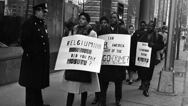 1961年2月11日、NYのベルギー領事館前で反ベルギー、ルムンバ支持のプラカードを掲げて抗議する人々 [AP Photo/Jacob Harris]
